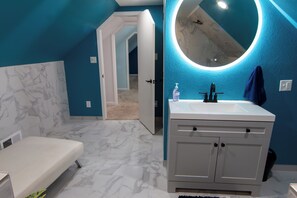 A modern bathroom with a white vanity, a round mirror with underglow lighting, and a blue accent wall.