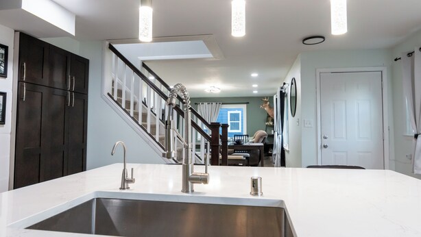 Une cuisine moderne dotée d’un grand îlot central, d’un évier en acier inoxydable et de luminaires suspendus.