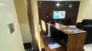 Un ufficio moderno con scrivania in legno, computer e televisore che mostra due persone.