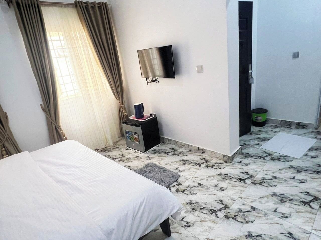 A hotel room with a bed, a TV mounted on the wall, a small table with a lamp, and a bathroom door.