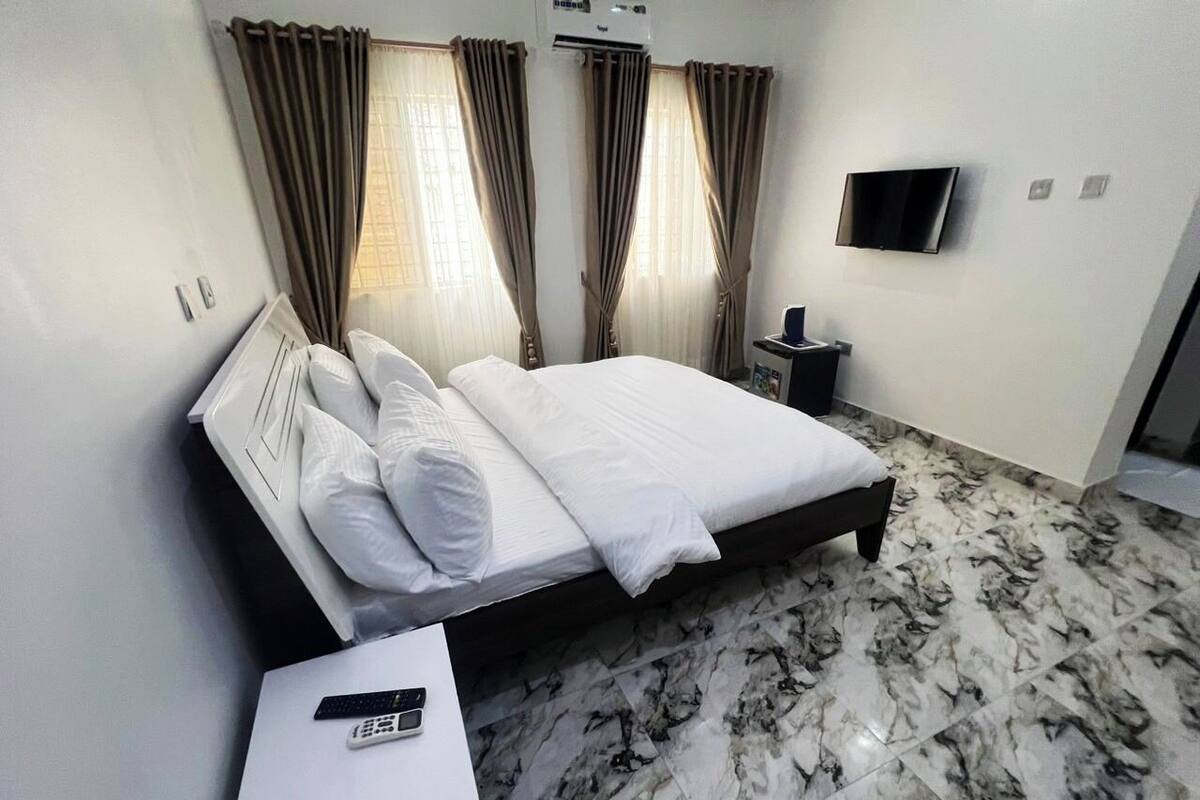 A hotel room with a bed, a TV mounted on the wall, a bedside table, and a remote control on the table.
