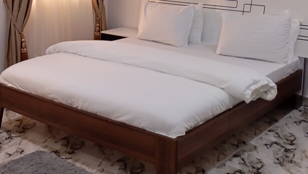 Un letto rifatto con lenzuola bianche in una stanza con pavimento effetto marmo.