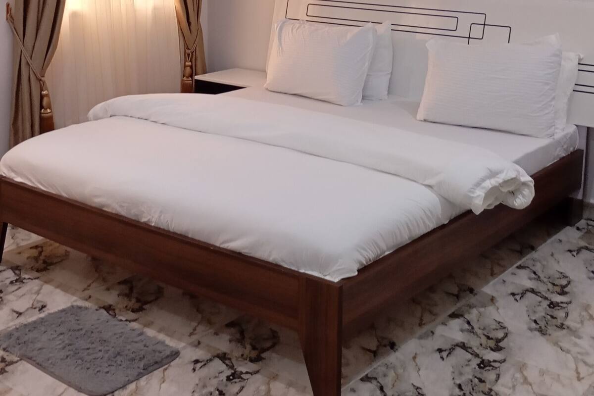 A neatly made bed with white linens in a room with a marble-patterned floor.