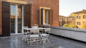 A balcony with a table and chairs, a brick building, and a window with shutters.
