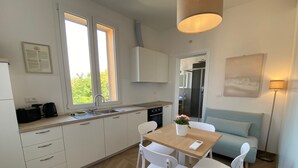 Een moderne keuken met witte kasten, een eettafel met stoelen, een koffiezetapparaat en een raam.