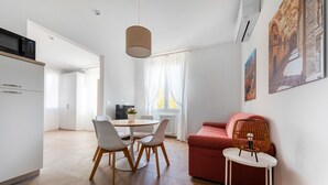 Un espace de vie moderne comprenant un coin repas, un canapé rouge, une petite table avec une lampe et des œuvres d’art accrochées au mur.