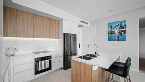A modern kitchen with white cabinetry, a black refrigerator, a built-in oven, and a wooden accent wall. - Solaris 610 overlooking the lake. (Forster)