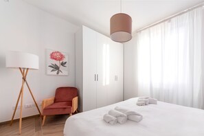 A hotel room with a bed, a chair, a wardrobe, and a floor lamp.