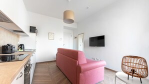 Une cuisine moderne avec un canapé rouge, un téléviseur fixé au mur et un fauteuil en osier.