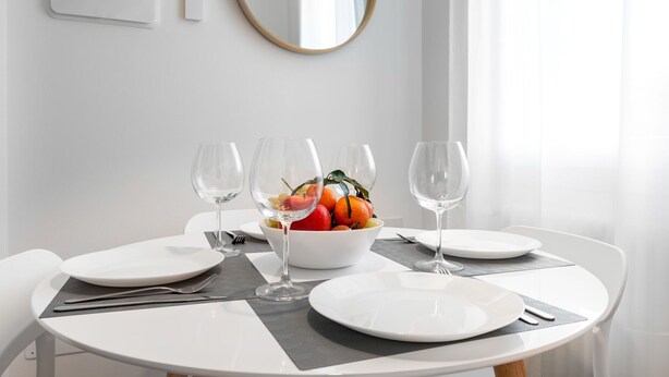 Une table à manger dressée avec de l’argenterie blanche, des verres à vin et un saladier rempli de fruits.