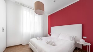Une chambre avec un lit blanc, un mur d’accent rouge et un plancher en bois.