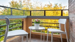 Un balcon avec deux chaises blanches, une petite table ronde et un pot de fleurs orné de fleurs roses.