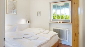 A bedroom with a bed, a window with a view, a radiator, and a wall-mounted light fixture. - Herzlich Willkommen im Appartement Nepomuk (List auf Sylt)