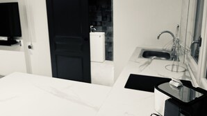Een moderne badkamer met een witte wastafel, spiegel en een zwarte deur die leidt naar een keuken.