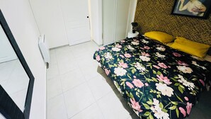 Een slaapkamer met een bloemenbedekking, een geel kussen, een schilderij aan de muur en een witte deur.