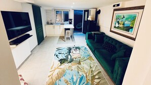 Een woonkamer met een groene bank, een bijzettafeltje en een aan de muur bevestigde televisie.