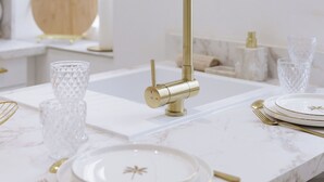 Una cocina moderna con grifo dorado, encimeras de mármol blanco y vajilla con detalles dorados.