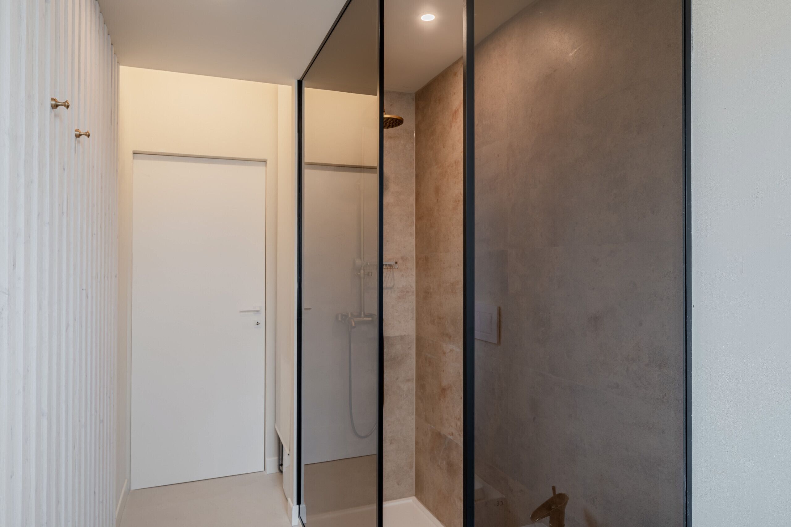 Une salle de bain moderne avec une douche à parois de verre, une porte blanche et un mur recouvert de carreaux beiges.
