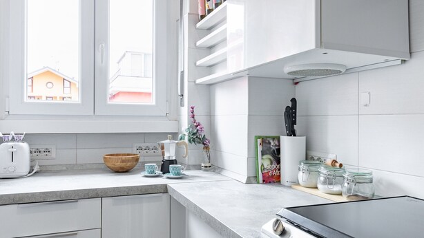 A modern kitchen with white cabinets, a built-in stove, and a window with a view of a house. - Golfo Aranci (Milano)