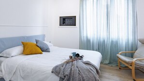A bedroom with a bed, pillows, a bedside table with a cup and a book, a chair, and a window with curtains. - Golfo Aranci (Milano)