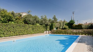 Et rektangulært swimmingpool med en klar, blå overflade, omgivet af en flisbelagt terrasse og en lav hæk.