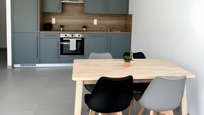 Een moderne keuken met grijze kastjes, een houten aanrechtblad en een eethoek met een houten tafel en stoelen.