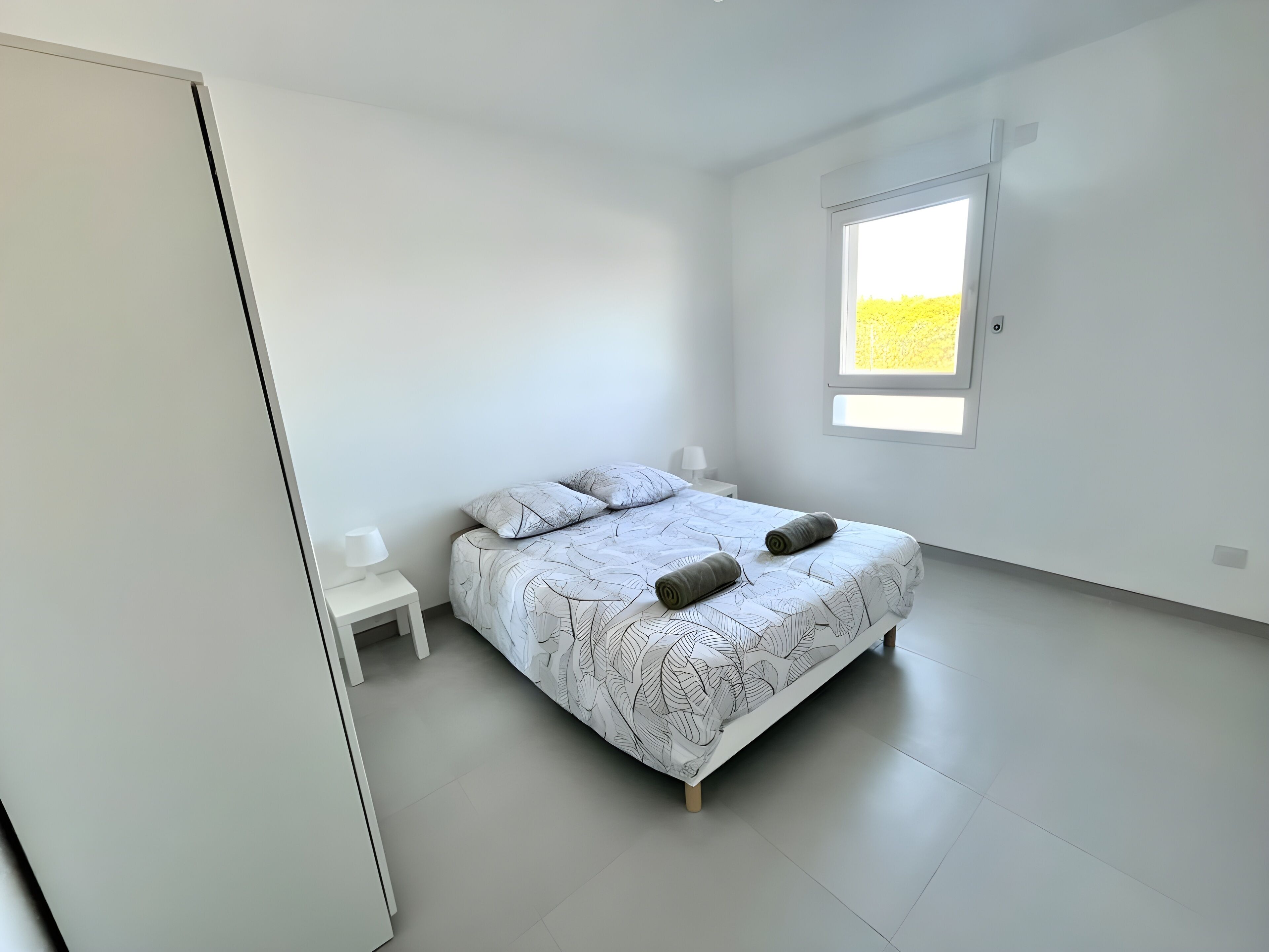 A minimalist bedroom with a bed, a nightstand, and a window.