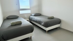 Een moderne, minimalistische slaapkamer met twee enkele bedden, een nachtkastje, een raam met uitzicht en een effen witte muur.