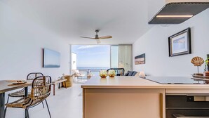 A modern kitchen with a central island, dining area with chairs, and a view of the sea.