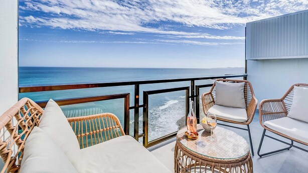 A balcony with wicker furniture, a glass table, and a view of the ocean.