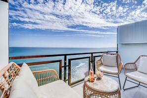 Ein Balkon mit Korbmöbeln, einem Glastisch und Blick aufs Meer.