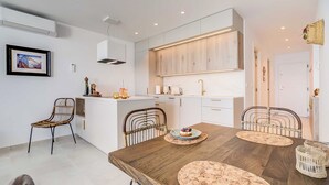 A modern kitchen with white cabinetry, a wooden island, and a dining area with a wooden table and woven chairs.