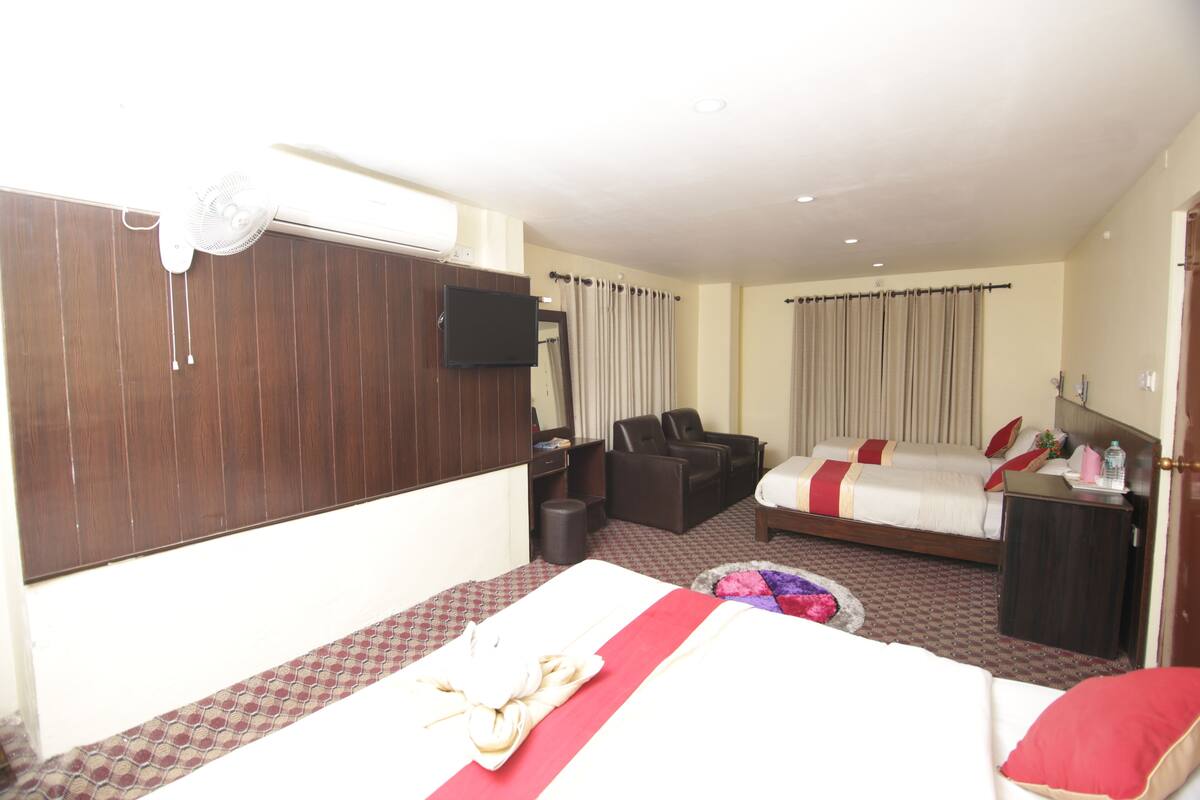A hotel room with a bed, a desk, a chair, a TV, and a window with curtains.