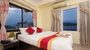 A hotel room with a large bed, a bedside table with a phone and a plant, and a window with curtains. - Hotel Nomad Inn (Pokhara)