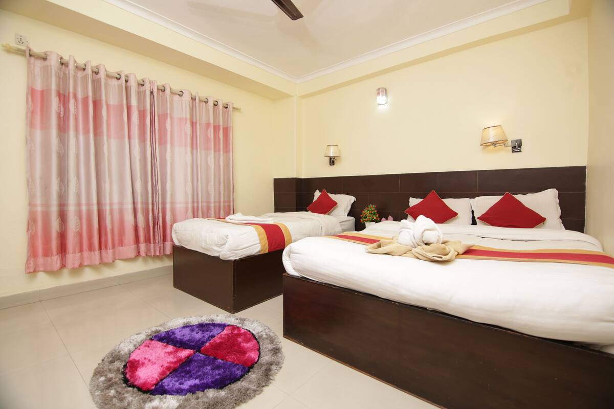 A hotel room with two beds, a small table, a colorful rug, and curtains.