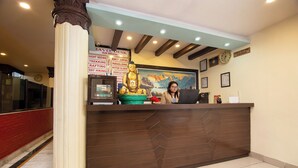 A reception desk with a clock, a Buddha statue, and a sign listing services like trekking and rafting. - Hotel Nomad Inn (Pokhara)