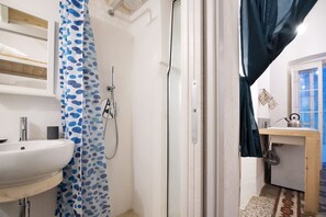 Bathroom features a shower area with a handheld showerhead, a sink with a faucet, and a soap dispenser.