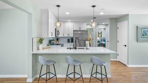 Una cocina moderna con una isla grande, taburetes de bar e iluminación colgante.