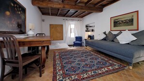 Una sala de estar acogedora con techo de madera, una mesa de comedor con sillas, un sofá, un tapete estampado y un cuadro en la pared.