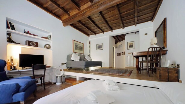 Un dormitorio con cama, escritorio con computadora, silla, sofá y mesa de comedor con sillas.