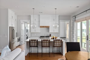 A modern kitchen with white cabinets, a central island with bar stools, stainless steel appliances, and pendant lighting. - Pet-Friendly + Pizza Oven + Walk to Moreland Amenities (Bluffton)