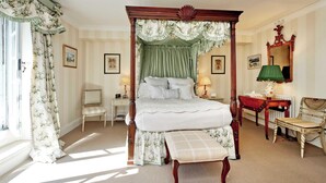 Een hemelbed met baldakijn, een nachtkastje met lamp, een stoel, en een spiegel aan de muur.