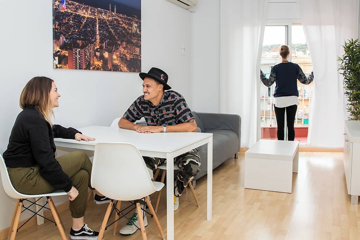 A modern meeting room with a white table, two chairs, a grey sofa, and a large cityscape painting on the wall.