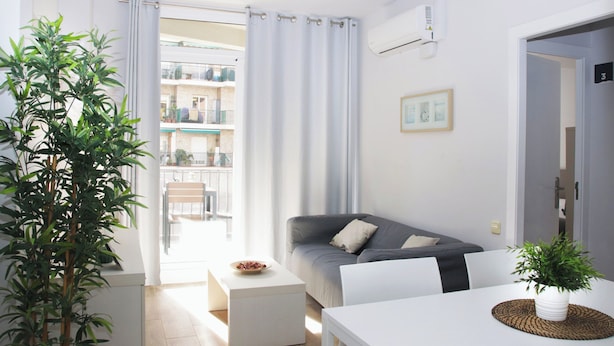 A modern living room with a grey sofa, a white dining table, and a potted plant. - Sant Jordi Apartments Sagrada Familia (Barcelona)