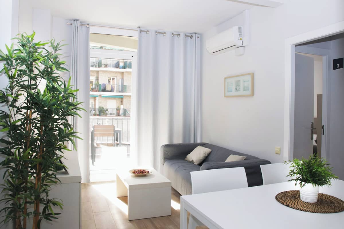 A modern living room with a grey sofa, a white dining table, and a potted plant.
