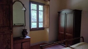 A bedroom with a wooden bed, a dresser, a mirror, and a window with a view of trees.