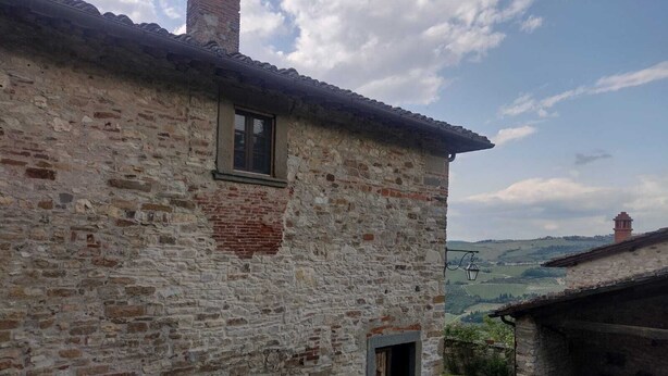 A rustic stone building with a small window and a door, surrounded by a rural landscape.
