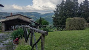 A rustic stone building with a thatched roof, surrounded by a wooden fence and lush greenery.
