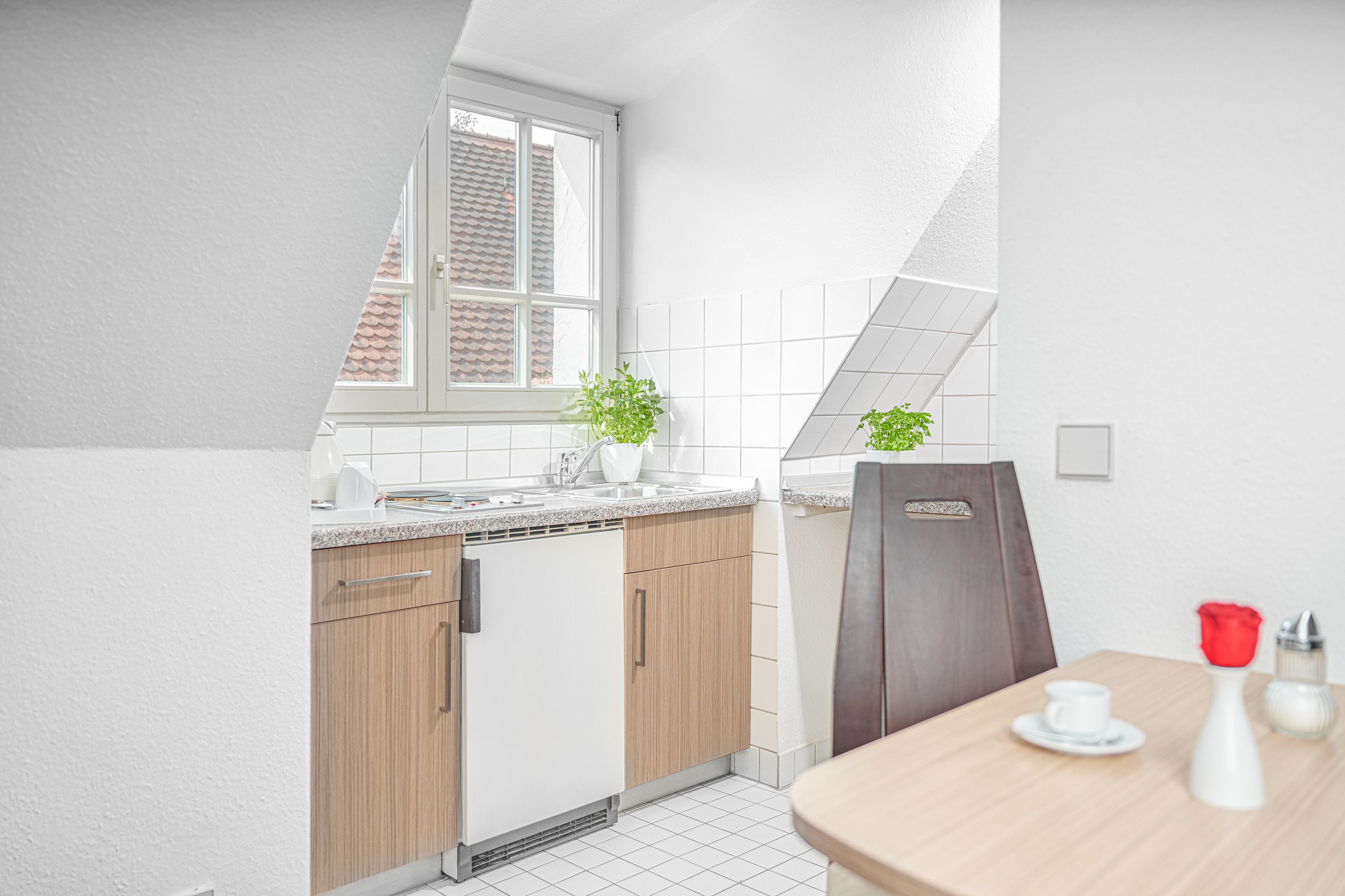 A modern kitchen with white cabinets, a wooden countertop, a window with a view, and a dining area with a table and chairs.