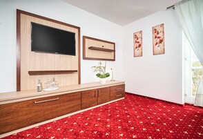 Una habitación con una televisión de pantalla plana grande montada en un mueble de madera, una planta pequeña en maceta y dos cuadros en la pared.